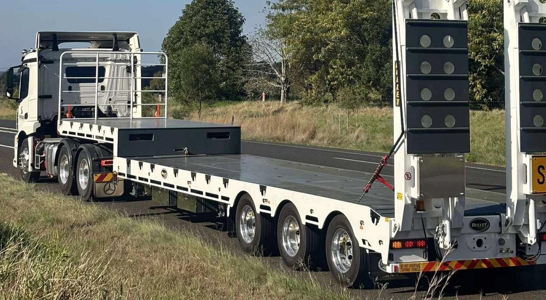 a white drop deck trailer attached to a white semi truck.
